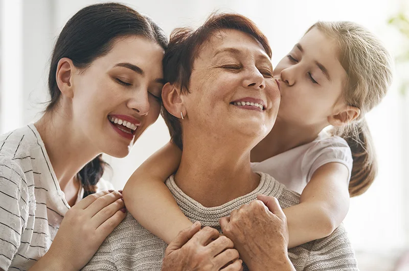 Três gerações de uma família abraçadas e sorrindo